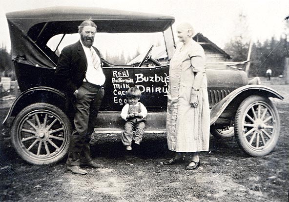 Photo of Harry and Louisa Buzby with very young Jim Spencer, and their car with 'Buzby's Dairy, real buttermilk, milk, cream, eggs' painted on the side.