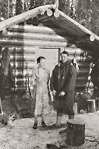 Photo of Bob and Tiny Buzby posing in front of a log cabin